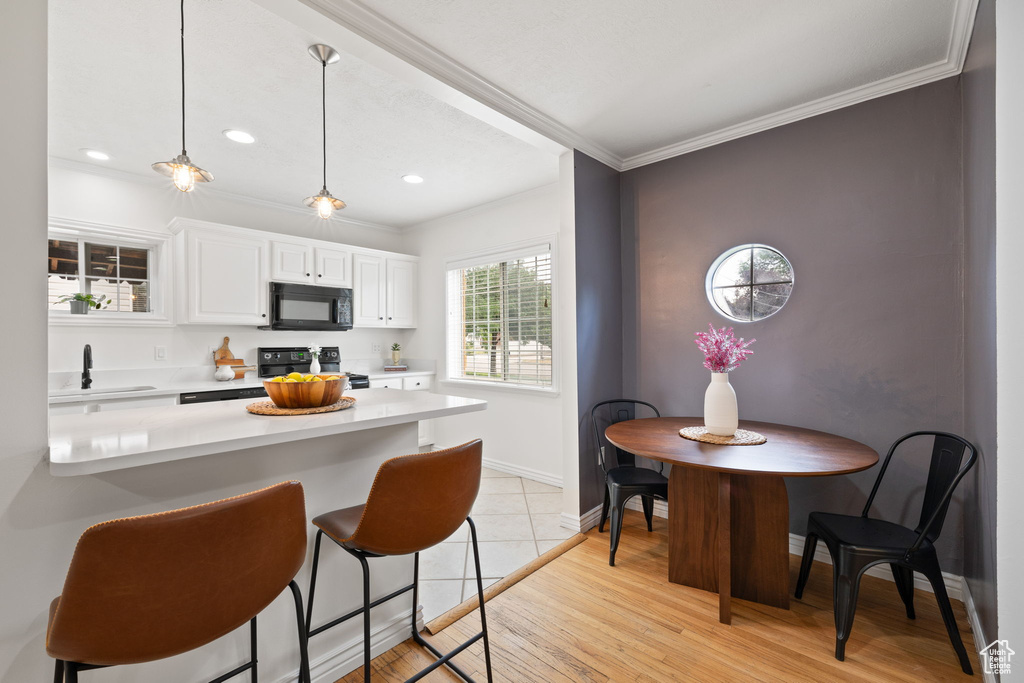 Kitchen with black microwave, range with electric stovetop, light countertops, a kitchen bar, and white cabinets