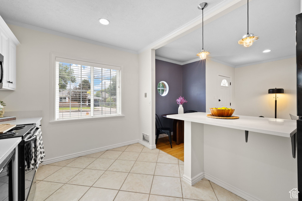 Kitchen with electric range oven, crown molding, light countertops, hanging light fixtures, and white cabinets