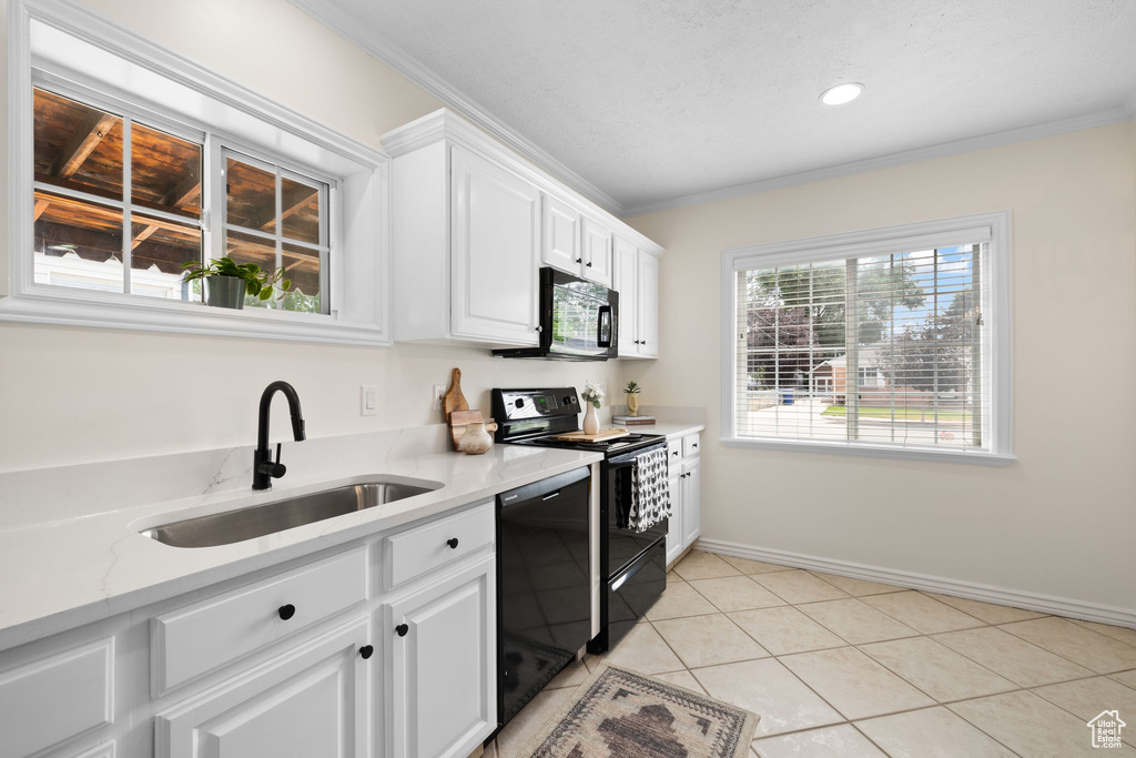 Kitchen featuring black appliances, crown molding, white cabinets, light tile patterned floors, and light stone counters