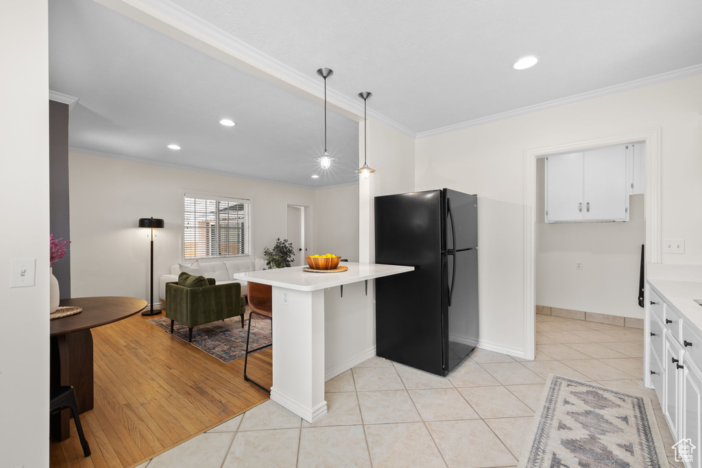 Kitchen featuring freestanding refrigerator, a breakfast bar area, light countertops, crown molding, and light tile patterned floors