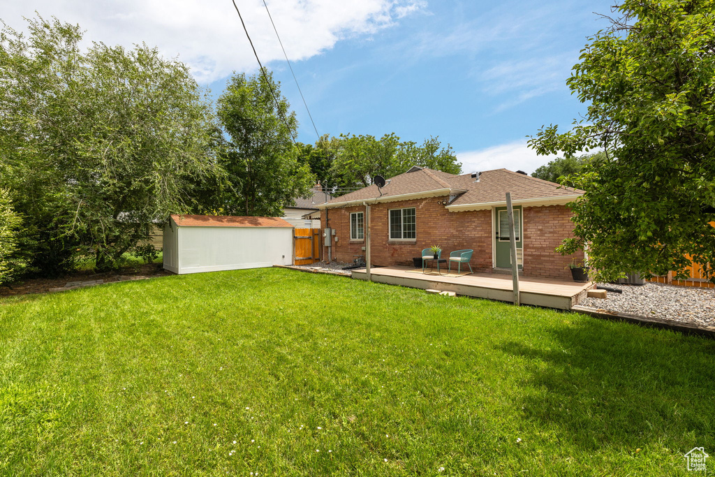 Rear view of house featuring a wooden deck, brick siding, a shingled roof, and a storage shed