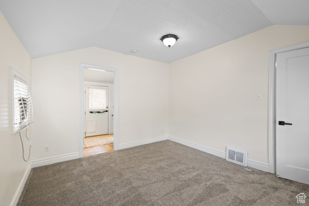 Empty room with vaulted ceiling and carpet