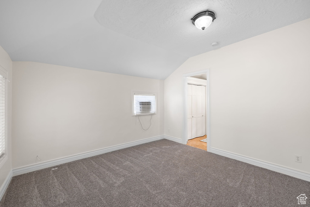 Carpeted spare room featuring vaulted ceiling and a textured ceiling