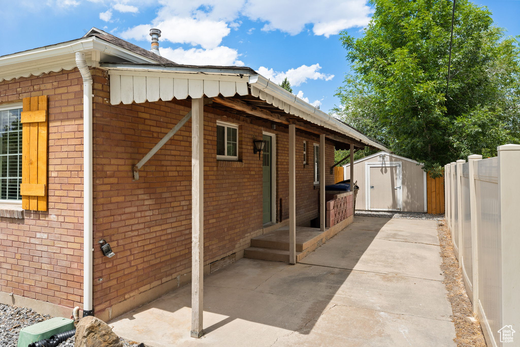 View of side of home with a storage unit, brick siding, and a patio area