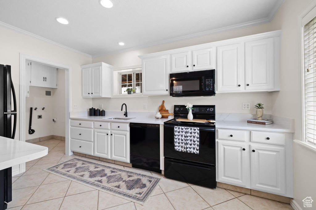 Kitchen with black appliances, light countertops, white cabinetry, crown molding, and plenty of natural light