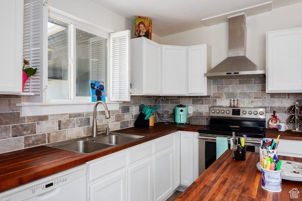 Kitchen featuring wooden counters, wall chimney range hood, stainless steel electric range oven, white dishwasher, and white cabinets