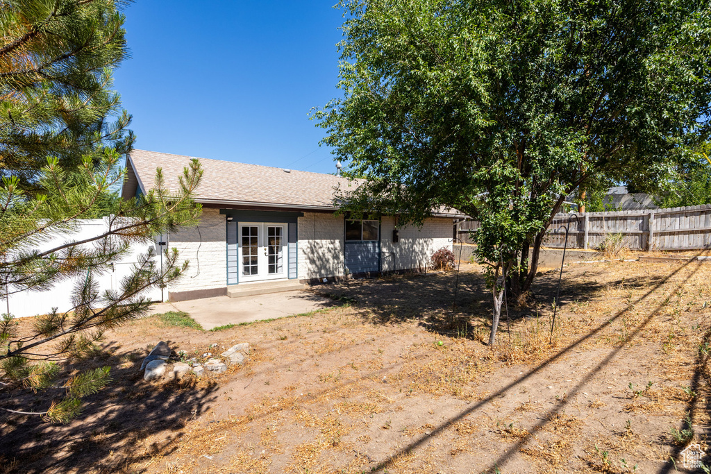 Back of house featuring french doors, a fenced backyard, a patio area, roof with shingles, and brick siding