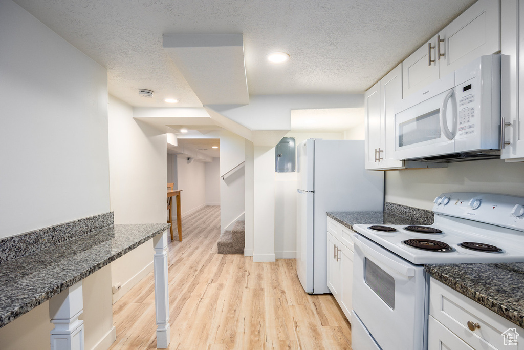 Kitchen with white appliances, light wood-type flooring, white cabinets, dark stone counters, and a textured ceiling