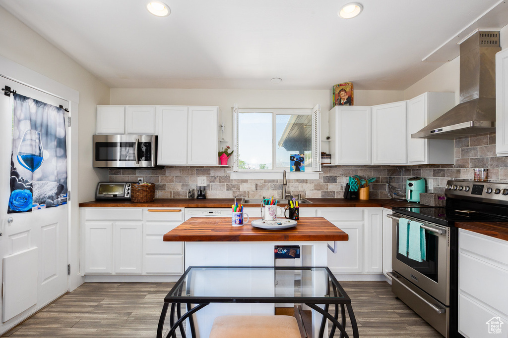 Kitchen with appliances with stainless steel finishes, wall chimney exhaust hood, butcher block counters, recessed lighting, and wood finished floors
