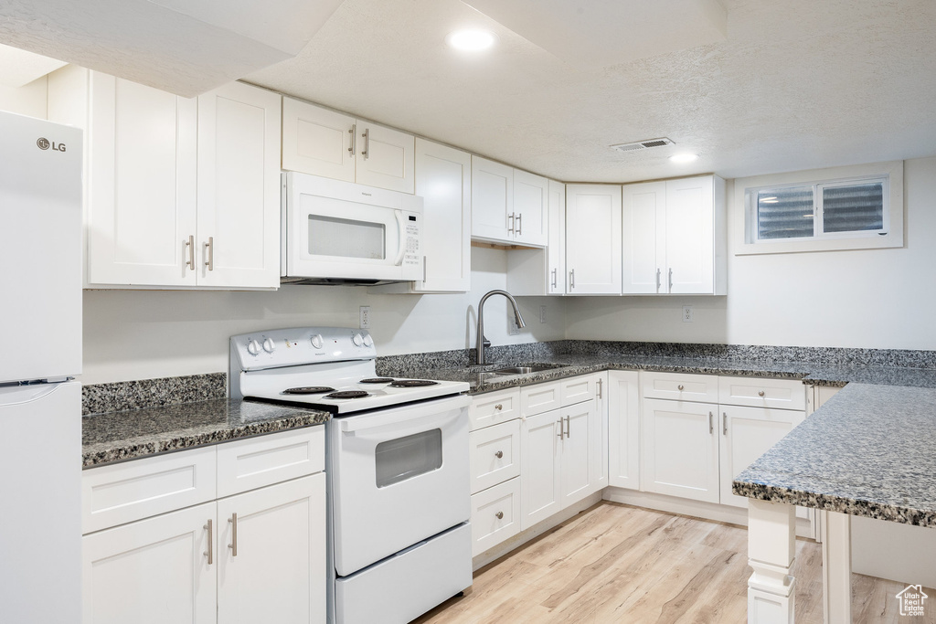 Kitchen featuring white appliances, light wood-style flooring, white cabinetry, dark stone counters, and recessed lighting