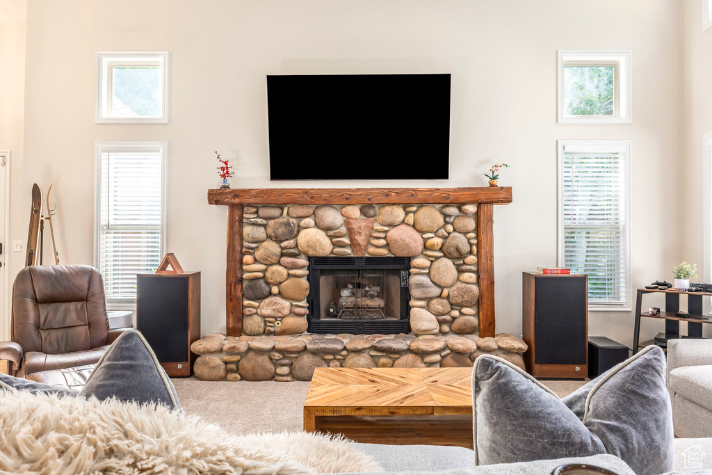Living room featuring a stone fireplace, healthy amount of natural light, and carpet flooring