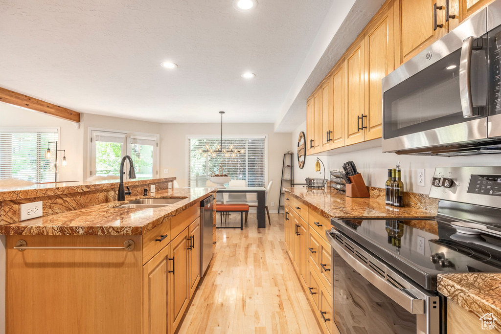 Kitchen with appliances with stainless steel finishes, recessed lighting, light wood-type flooring, light stone countertops, and a chandelier