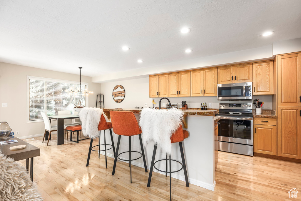 Kitchen featuring appliances with stainless steel finishes, a breakfast bar, light wood-style floors, recessed lighting, and pendant lighting