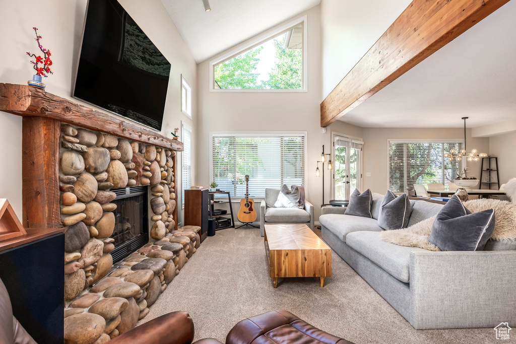 Carpeted living area with a stone fireplace, plenty of natural light, a chandelier, and a high ceiling
