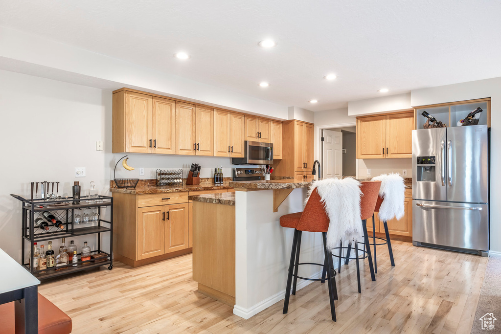 Kitchen with appliances with stainless steel finishes, light brown cabinetry, light wood-style flooring, recessed lighting, and a breakfast bar area