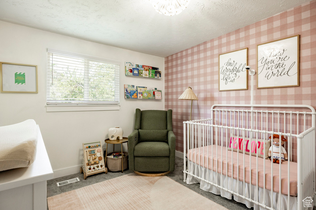 Carpeted bedroom with a nursery area, wallpapered walls, and a textured ceiling