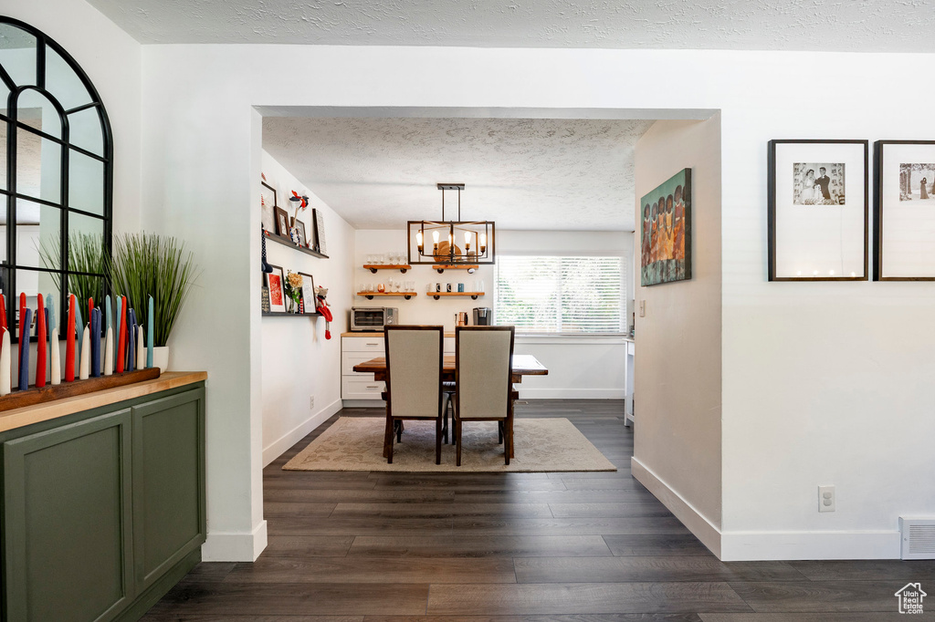 Dining area with a textured ceiling, dark wood-style floors, and a chandelier