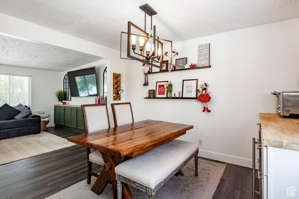 Dining room with dark wood-type flooring, a chandelier, and a textured ceiling