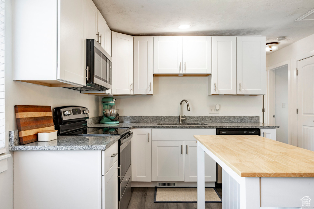 Kitchen with stainless steel appliances, white cabinetry, butcher block countertops, and dark wood finished floors