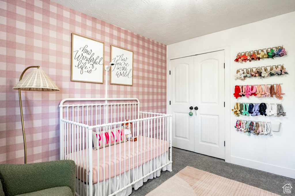 Carpeted bedroom with wallpapered walls, a closet, a nursery area, and a textured ceiling