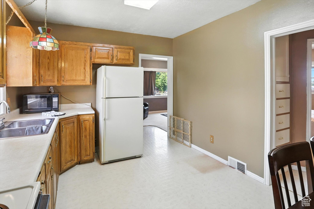 Kitchen with freestanding refrigerator, black microwave, light countertops, and brown cabinets