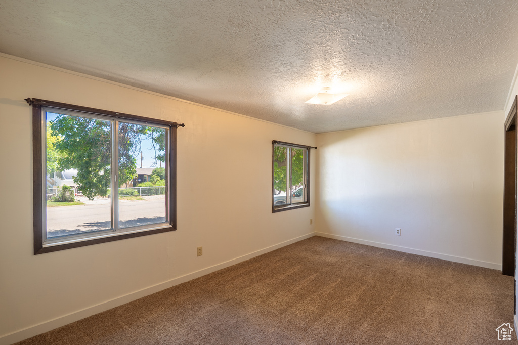 Empty room with plenty of natural light, dark colored carpet, and a textured ceiling