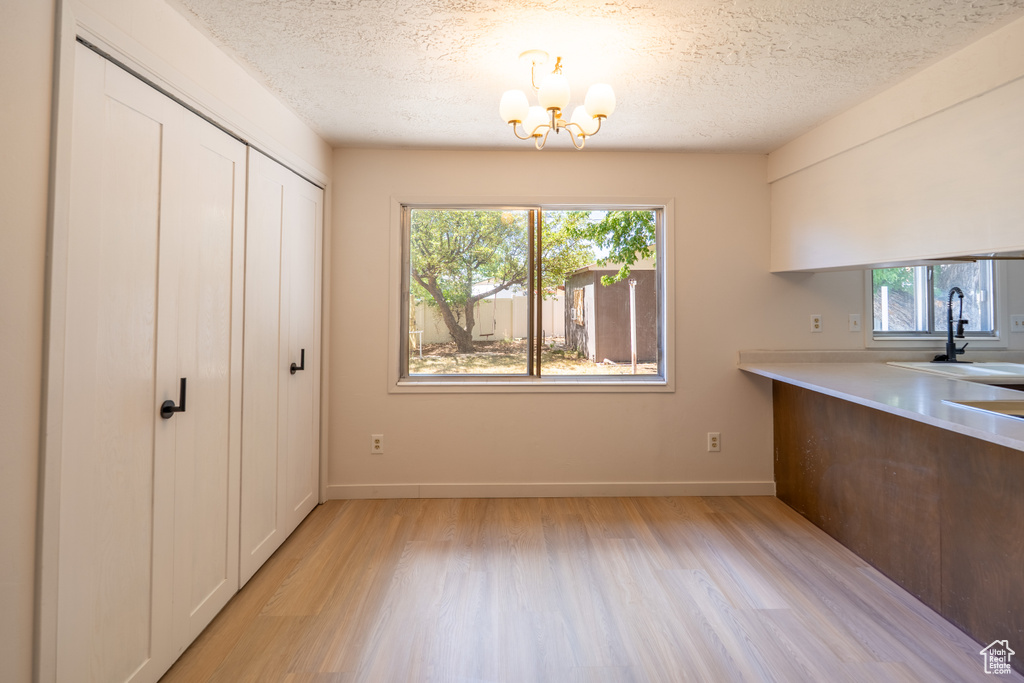 Unfurnished dining area featuring healthy amount of natural light, light wood finished floors, a chandelier, and a textured ceiling
