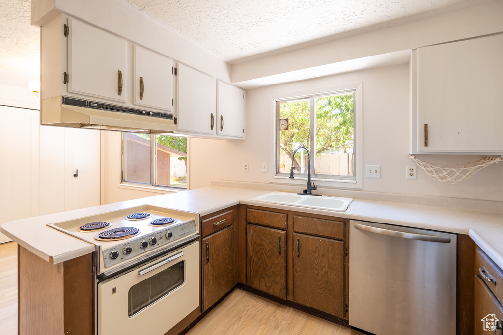 Kitchen with dishwasher, white electric range oven, under cabinet range hood, a peninsula, and light countertops