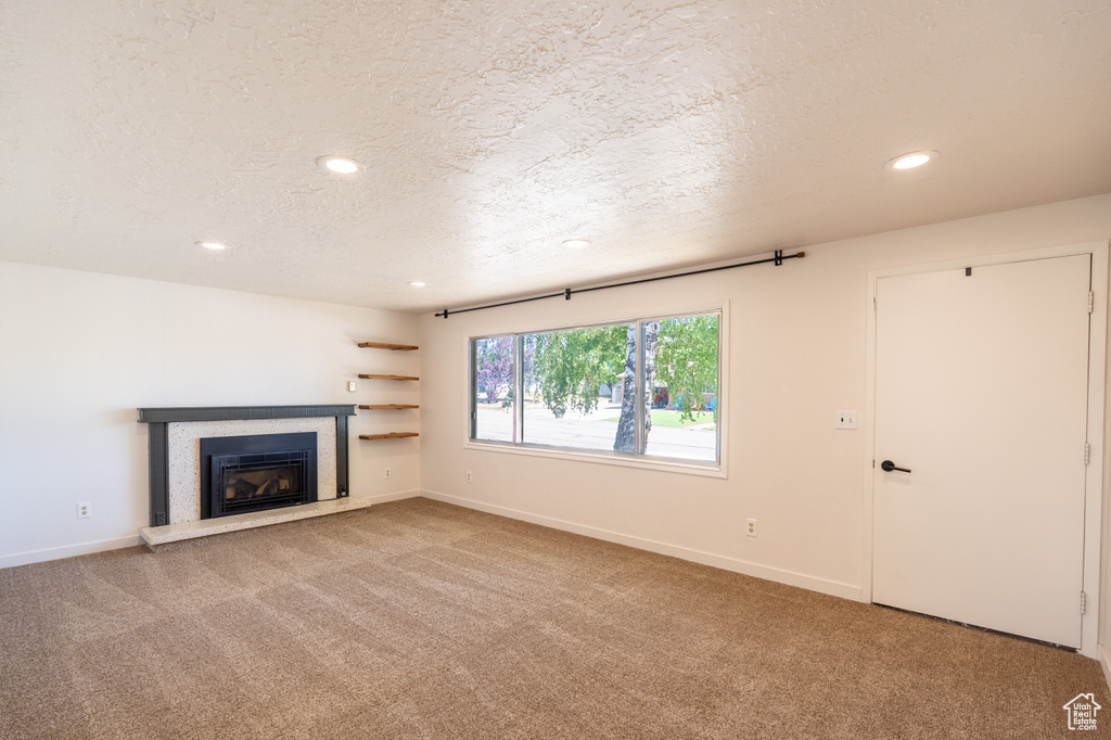 Unfurnished living room featuring a textured ceiling, recessed lighting, carpet flooring, and a glass covered fireplace