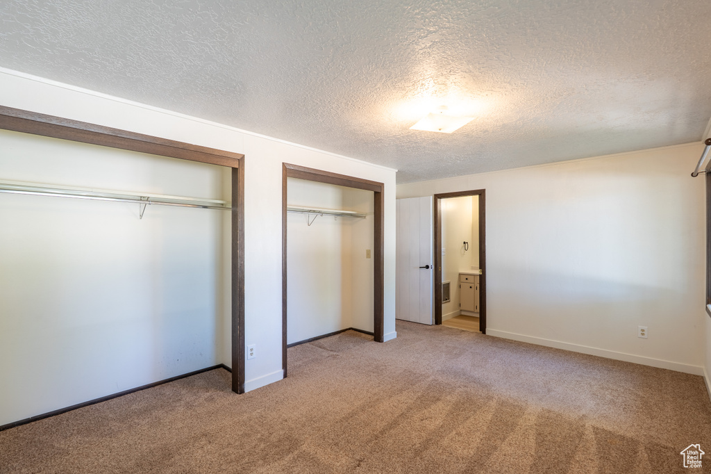 Unfurnished bedroom with multiple closets, light carpet, and a textured ceiling