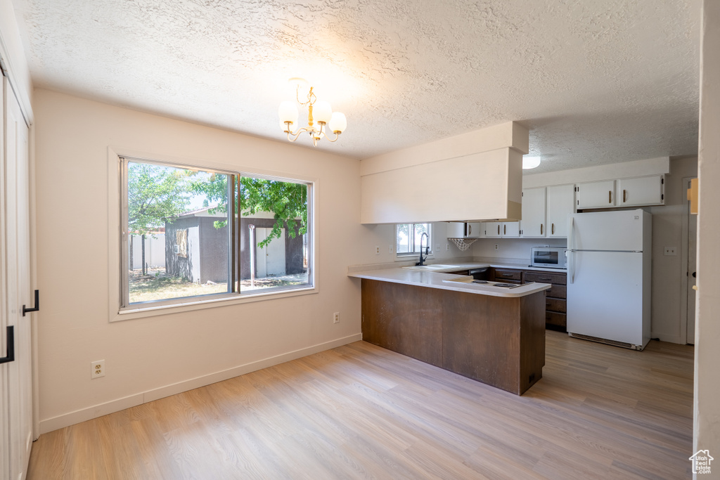 Kitchen with white appliances, a peninsula, a textured ceiling, a chandelier, and light wood-style flooring
