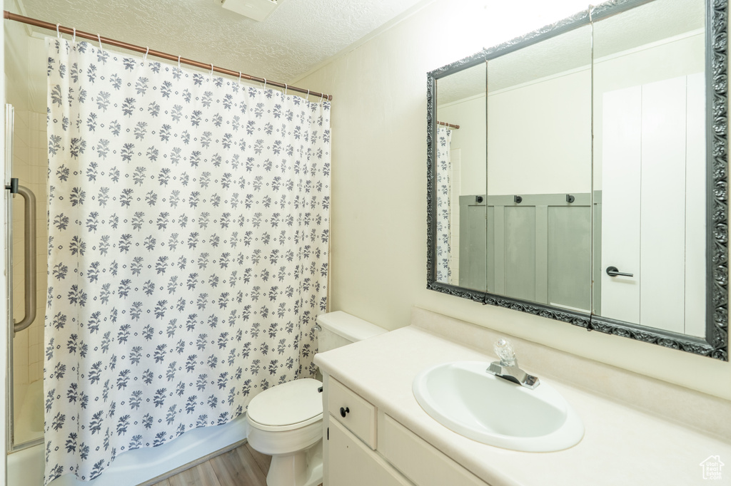 Bathroom with a textured ceiling, vanity, shower / bath combo with shower curtain, and wood finished floors