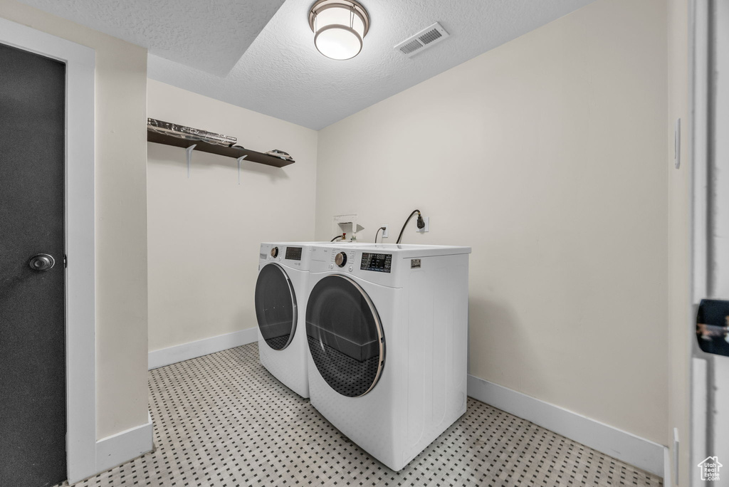Laundry room featuring separate washer and dryer, light flooring, and a textured ceiling