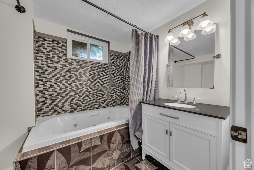 Bathroom featuring a combined bath / shower with jetted tub, vanity, and a textured ceiling