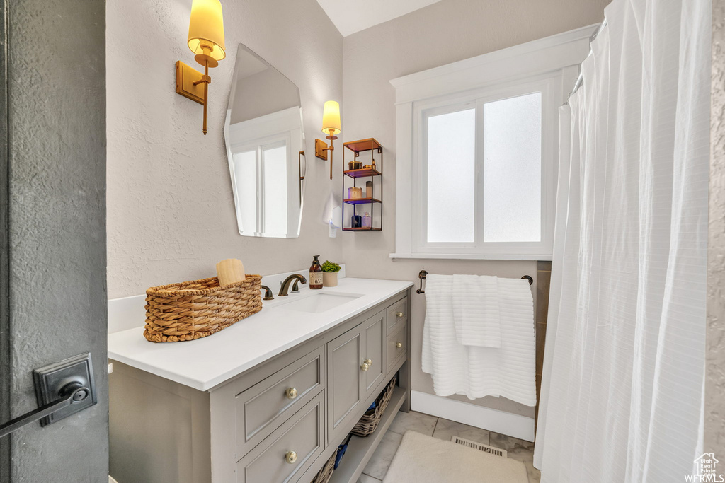 Bathroom featuring vanity, marble look tiles, and a textured wall