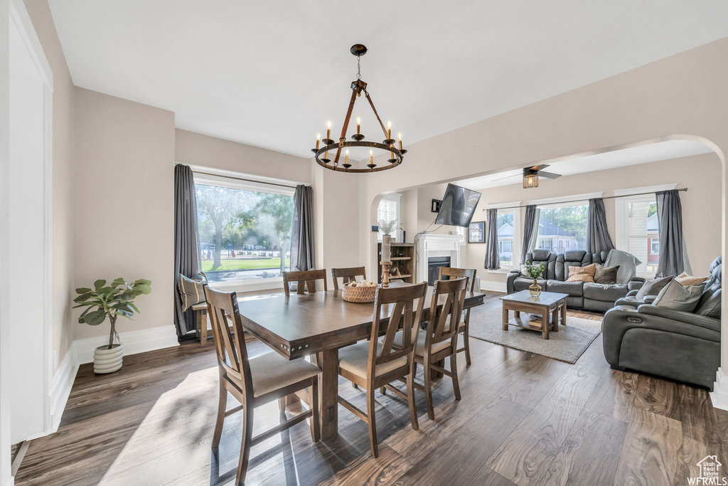 Dining area featuring arched walkways, dark wood-type flooring, a fireplace, a chandelier, and ceiling fan