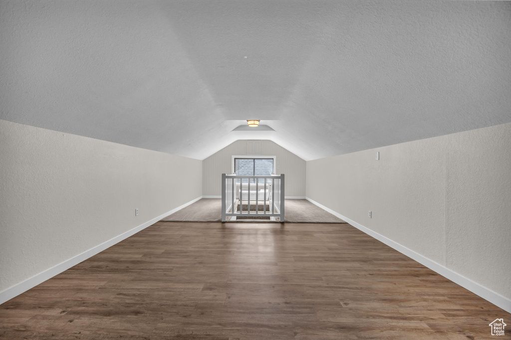 Additional living space featuring lofted ceiling, dark wood-type flooring, a textured wall, and a textured ceiling