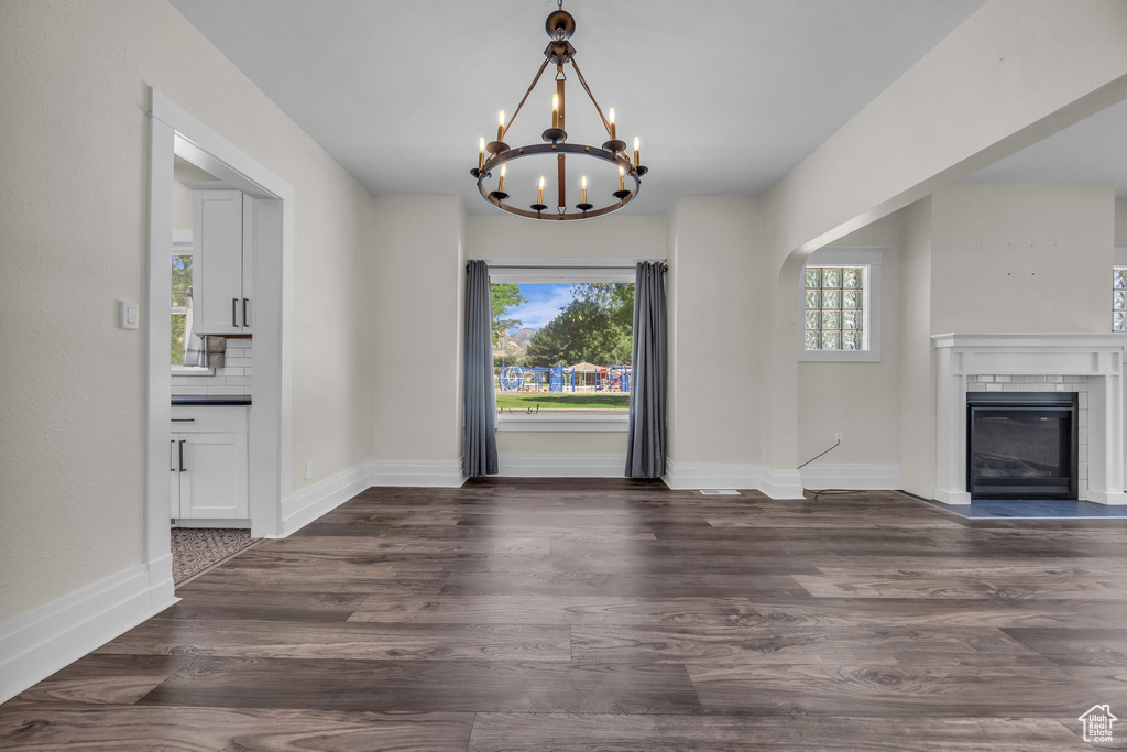 Unfurnished dining area featuring plenty of natural light, a chandelier, a glass covered fireplace, and dark wood-style floors