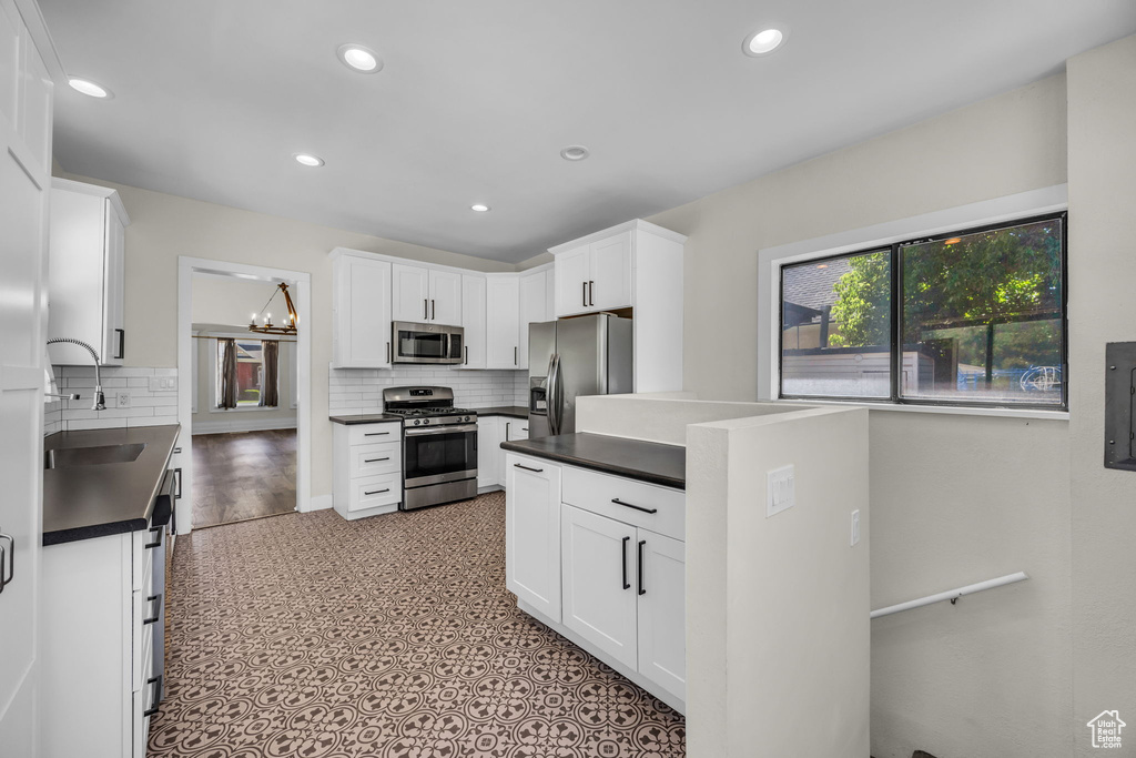Kitchen featuring stainless steel appliances, dark countertops, decorative backsplash, recessed lighting, and white cabinetry