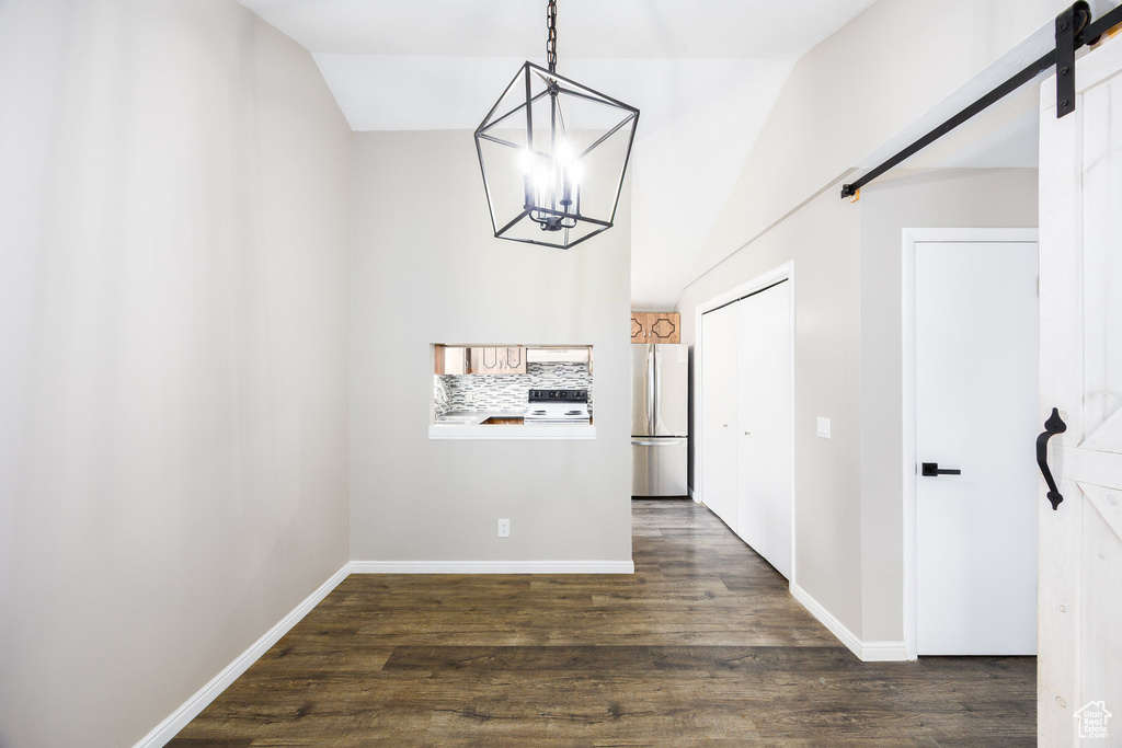 Unfurnished dining area featuring a chandelier, a barn door, dark wood-style flooring, and lofted ceiling