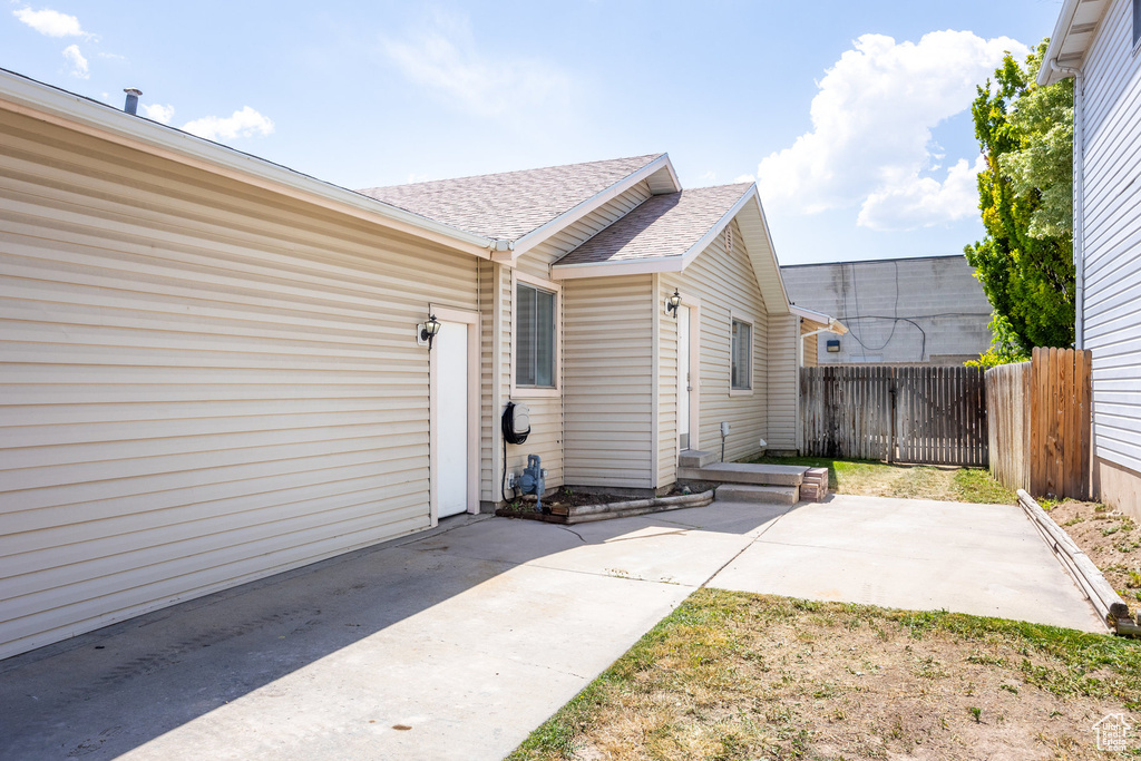Property entrance with a shingled roof, a patio, and driveway