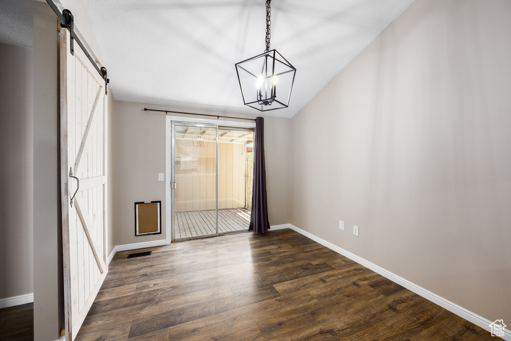 Unfurnished dining area with a barn door, dark wood finished floors, a chandelier, healthy amount of natural light, and lofted ceiling