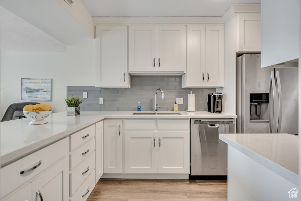 Kitchen with stainless steel appliances, white cabinetry, tasteful backsplash, and light wood-style flooring