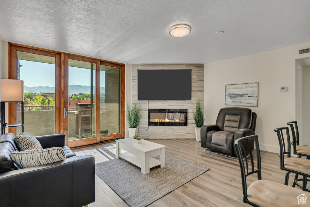 Living area featuring light wood finished floors, a glass covered fireplace, a textured ceiling, and floor to ceiling windows