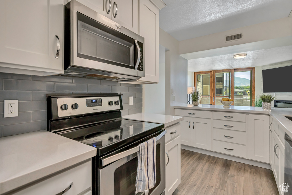 Kitchen with stainless steel appliances, light countertops, tasteful backsplash, light wood-type flooring, and white cabinets