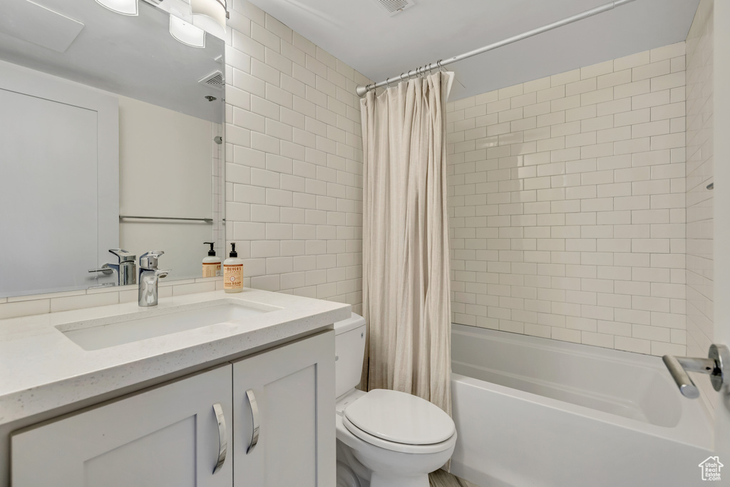 Full bathroom with vanity, shower / bath combo with shower curtain, and tile walls