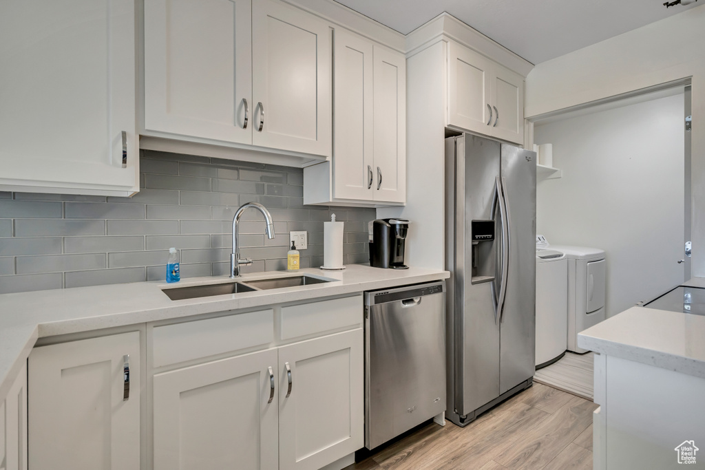Kitchen featuring appliances with stainless steel finishes, independent washer and dryer, backsplash, and white cabinets