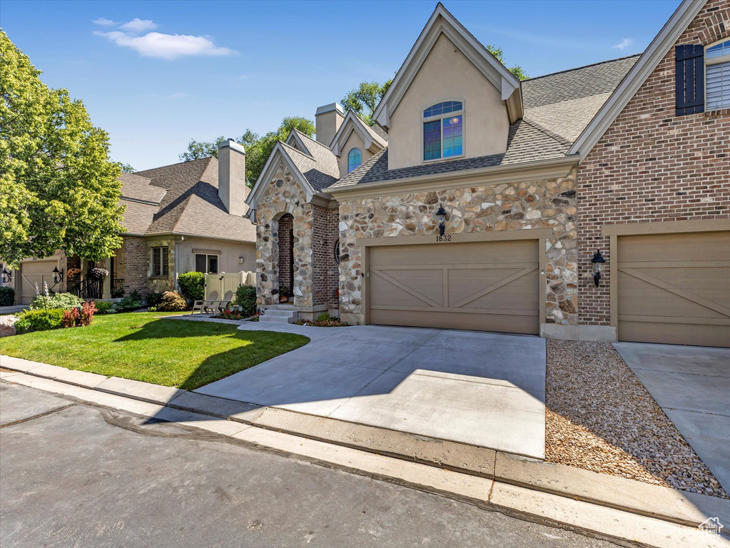French country inspired facade featuring driveway, a front yard, stone siding, and stucco siding