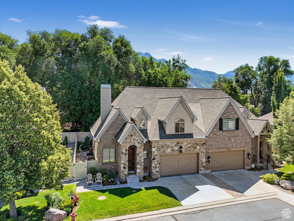 French country inspired facade featuring a garage, driveway, a chimney, a mountain view, and brick siding