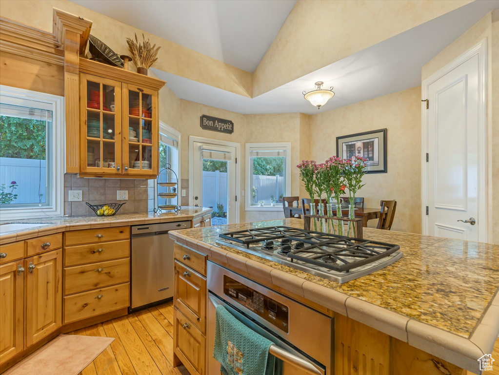 Kitchen featuring stainless steel appliances, vaulted ceiling, light wood finished floors, plenty of natural light, and tile counters